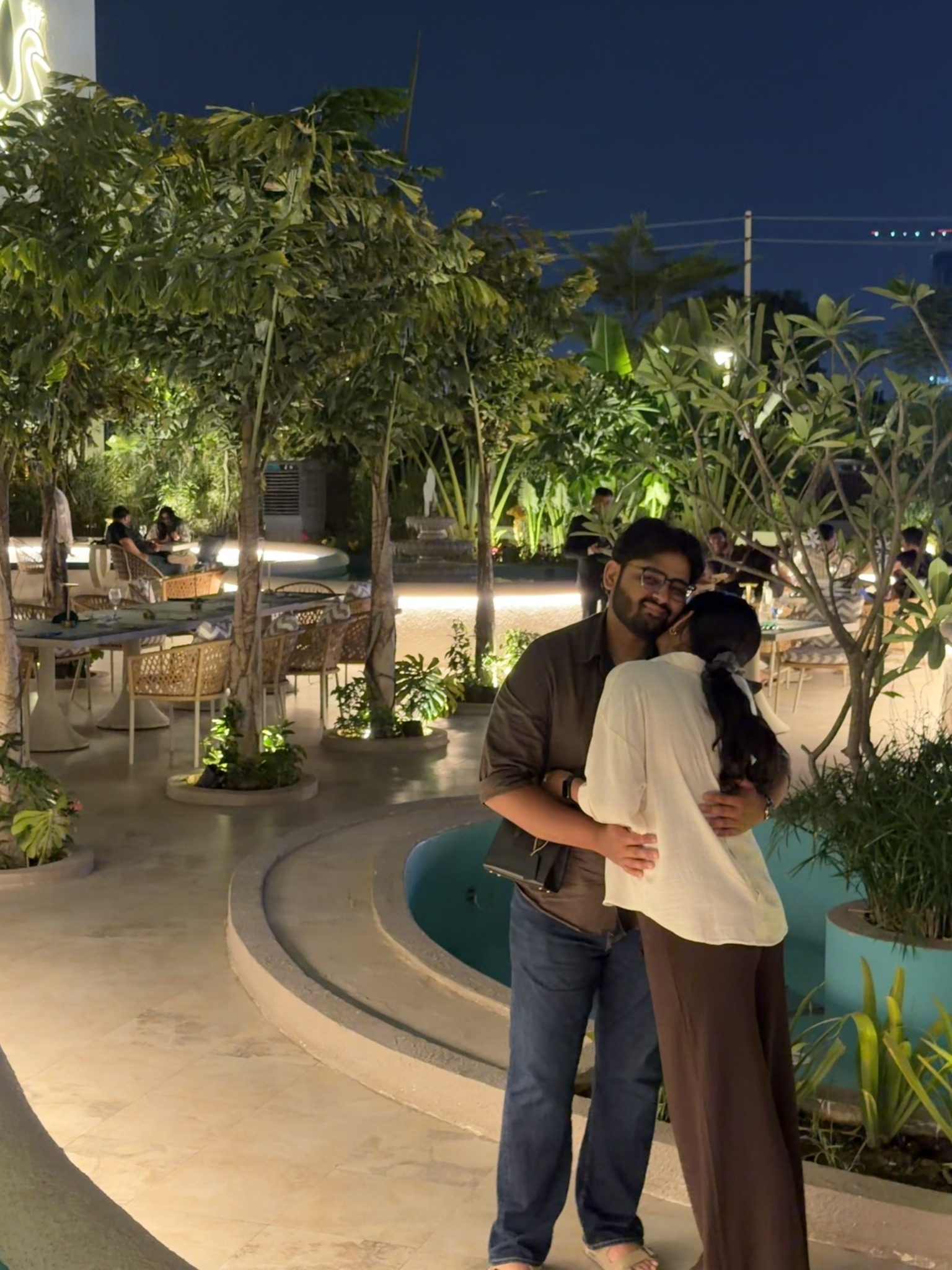 Dev and Dhimahi embracing in an outdoor garden at night